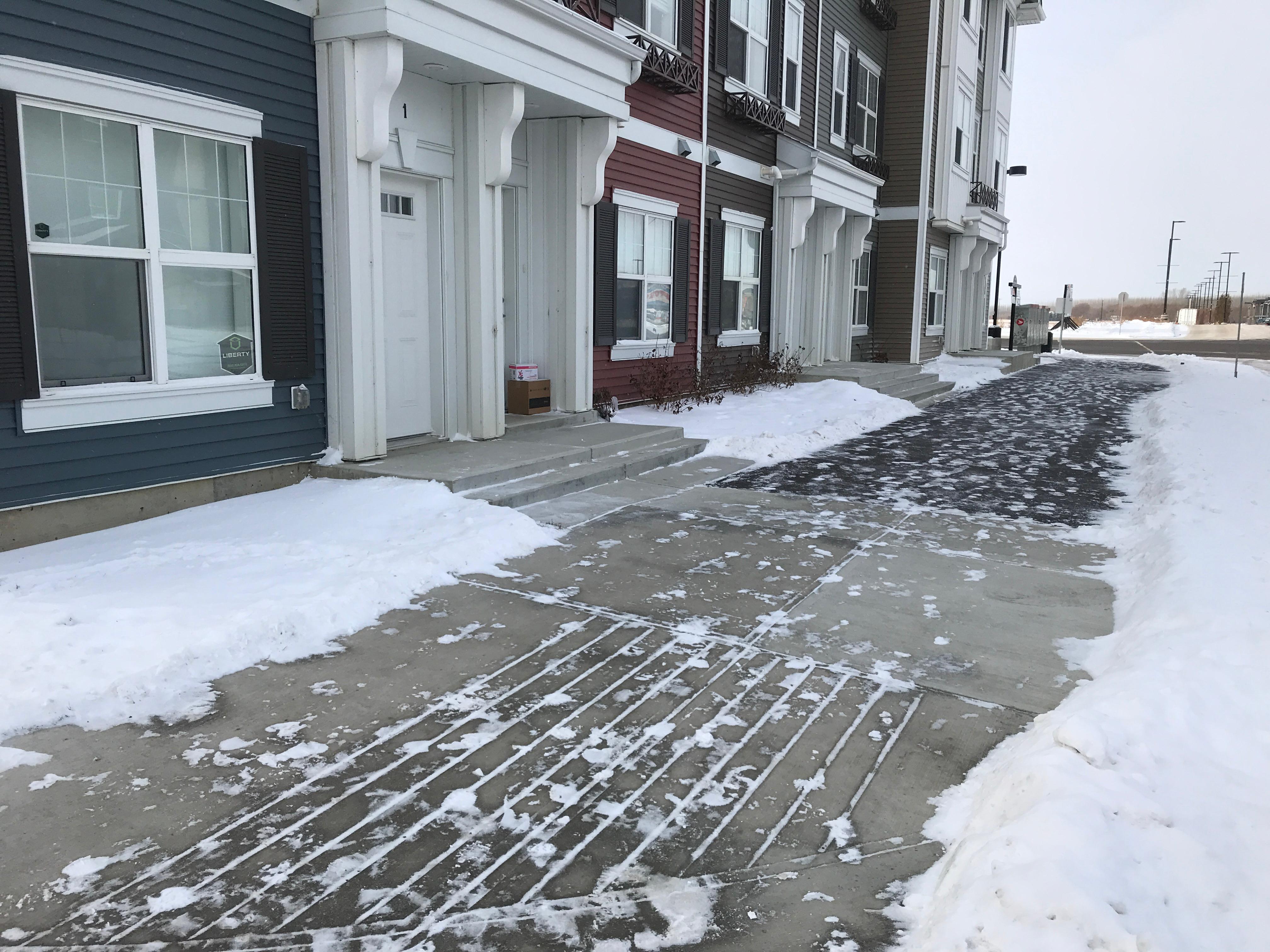 Row of townhouse fronts with cleared walkways and driveways in winter